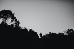 two people standing on top of a hill with trees in the foreground and dark sky behind them