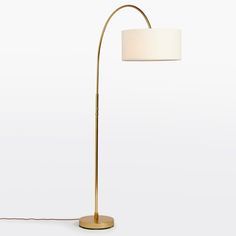 a floor lamp with a white shade on the top and a gold base, in front of a white background