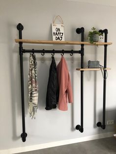 a coat rack with two coats hanging from it's sides and some plants on the other side