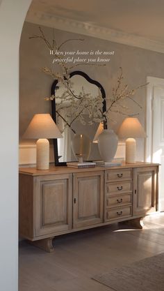 a vase with flowers on top of a dresser in front of a mirror and two lamps