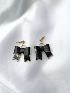 "These earrings are the perfect accessory to complete any outfit. The combination of black and gold gives a stylish and trendy look that will make you stand out from the crowd. The bow design adds a touch of femininity, while the leather material gives them a unique texture and feel. These earrings are lightweight and comfortable, making them perfect for all-day wear. Pair them with a little black dress for a classy evening look or wear them with a casual outfit to add a touch of elegance. These Black Bow Jewelry For Evening, Black Bow Jewelry Gift, Black Bow Jewelry For Gifts, Black Bow Jewelry For Gift, Black Bow Tie Jewelry For Party, Chic Black Earrings For Party, Black Jewelry With Ribbon For Evening, Black Ribbon Jewelry For Evening, Black Bow Earrings For Party