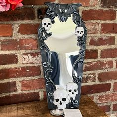 there is a mirror with skulls on it next to a brick wall and pink flowers