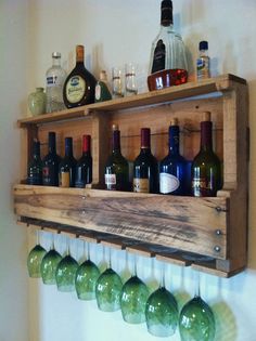 a wooden shelf filled with lots of bottles next to a wall mounted wine glass rack