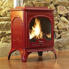 a red stove sitting on top of a wooden floor next to a stone wall and fire place