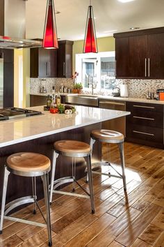 two stools sit at the center of a kitchen island with three pendant lights hanging over it