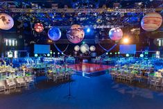 a large room filled with lots of tables covered in white and blue cloths next to space themed balloons