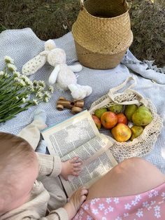 a baby is reading a book while sitting on a blanket with apples and pears