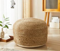 a large round jute ottoman on the floor next to a potted plant in a living room