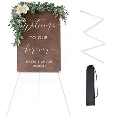 a welcome sign with greenery on it next to an easel