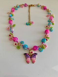 This charming beaded flower and multi bead necklace inspired by nature's beauty. Adorned with a delicate Enamel 20*15 mm  pink butterfly charm featuring a shimmering green leafs, dangling beaded flower beads, glass round beads and bicone beads, this piece captures the essence of femininity and elegance. The gold stainless steel chain adds a touch of sophistication. With a length of 15 inches and an additional 3-inch extender chain, this necklace offers versatility in styling. Whether it's day or Pink Flower Necklaces With Colorful Beads, Pink Flower-shaped Necklaces With Colorful Beads, Pink Flower Necklace With Colorful Beads, Whimsical Multicolor Flower Necklace, Adjustable Pink Flower Necklace With Colorful Beads, Pink Flower Necklace With Colorful Beads As Gift, Fairycore Multicolor Jewelry For Gifts, Multicolor Fairycore Jewelry For Gifts, Whimsical Pink Beaded Necklaces