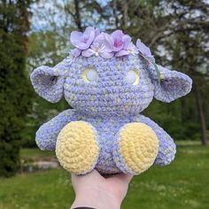 a hand holding up a crocheted stuffed animal with purple flowers on its head