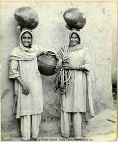 two women standing next to each other with baskets on their heads and one holding a pot