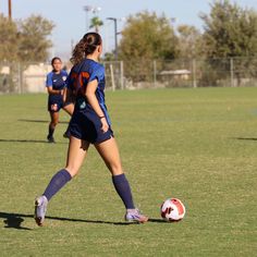 two girls are playing soccer on the field with one girl in blue is about to kick the ball