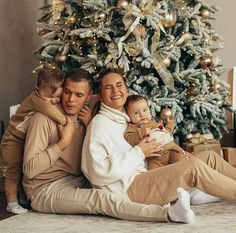 a man and woman are sitting in front of a christmas tree while holding their children