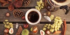 a cup of coffee sitting on top of a wooden table next to pine cones and nuts