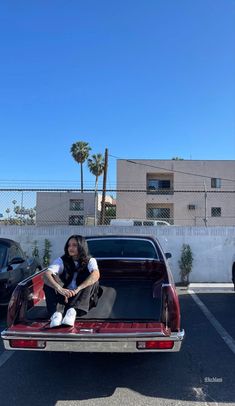 a woman sitting on the back of a car in a parking lot