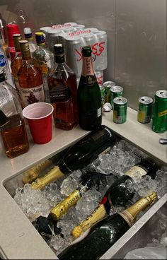 an open sink filled with lots of bottles and glasses on top of ice cubes