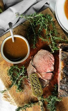 some meat and sauces are on a wooden plate with silverware next to it