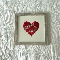 a heart made out of red flowers in a frame on a white quilted bed