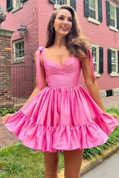 a woman standing in front of a pink house wearing a short dress with ruffles