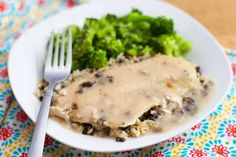 a white plate topped with meat covered in gravy next to broccoli