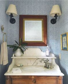 a bathroom with blue and white wallpaper has a wooden cabinet under the vanity mirror