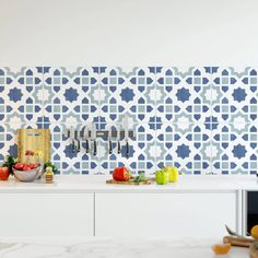 a kitchen with blue and white tiles on the wall next to a cutting board, knife, bowl of fruit and utensils