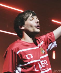 a man in a red shirt is holding his hand out to the side while singing into a microphone