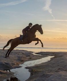 a man riding on the back of a brown horse next to a body of water