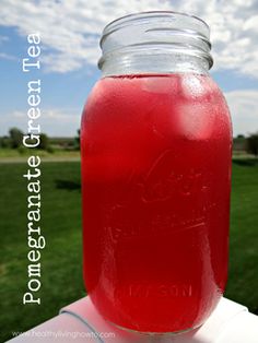 a mason jar filled with red liquid sitting on top of a white tablecloth in front of a green field