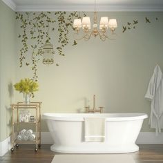 a white bath tub sitting under a chandelier next to a wall with vines on it