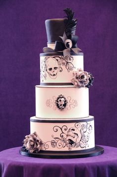 a three tiered wedding cake with skulls and flowers on the top, sitting on a purple tablecloth