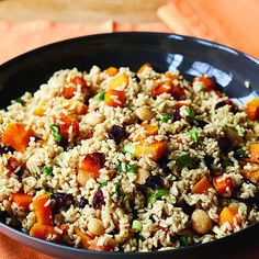 a black bowl filled with rice and vegetables on top of an orange napkin next to a wooden table