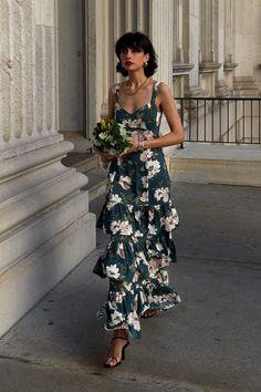 a woman is walking down the street with flowers in her hand and wearing a dress