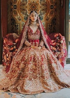 a woman sitting on top of a bed in a red and gold wedding dress with an elaborate