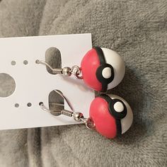 pair of red and white earrings with black eyes on ear hooks sitting next to a card