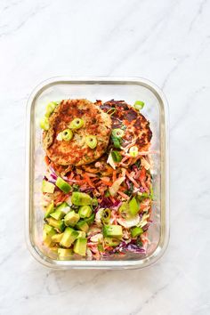 a meal in a plastic container with meat and veggies on the side, topped with avocado