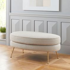 a white ottoman sitting on top of a hard wood floor next to a potted plant