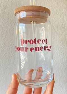 a hand holding a glass jar with the words protect your energy written on it in red