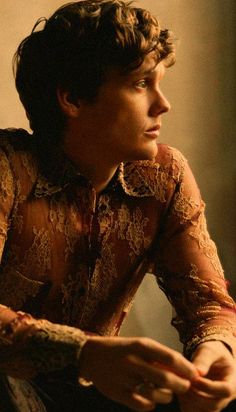 a young man sitting down with his hands on his knees and looking off to the side