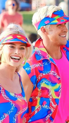 two people dressed in bright clothing and headbands smiling at the camera while standing next to each other