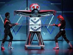 three people are performing on stage with a robot in the middle and one person standing behind them