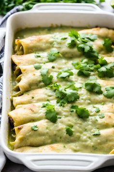 a white casserole dish filled with green enchiladas and garnished with cilantro