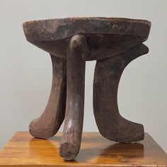 a wooden table topped with a metal object on top of a wooden block next to a white wall