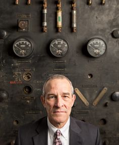 a man wearing a suit and tie standing in front of a wall with gauges on it