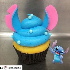 a cupcake with blue frosting and pink ears next to a small toy figurine