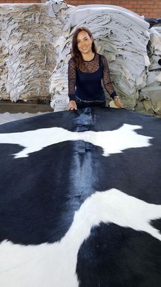 a woman standing on top of a black and white cow skin rug in front of stacks of paper