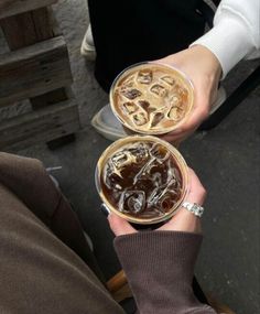 two people are holding up drinks in their hands, one is filled with ice and the other has chocolate