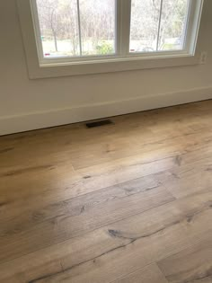 an empty room with wood flooring and two windows