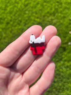 a hand holding a small red and white dog brooch in it's palm